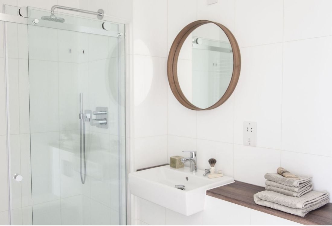 A modern, bright, bathroom featuring a sink, mirror, and shower area.