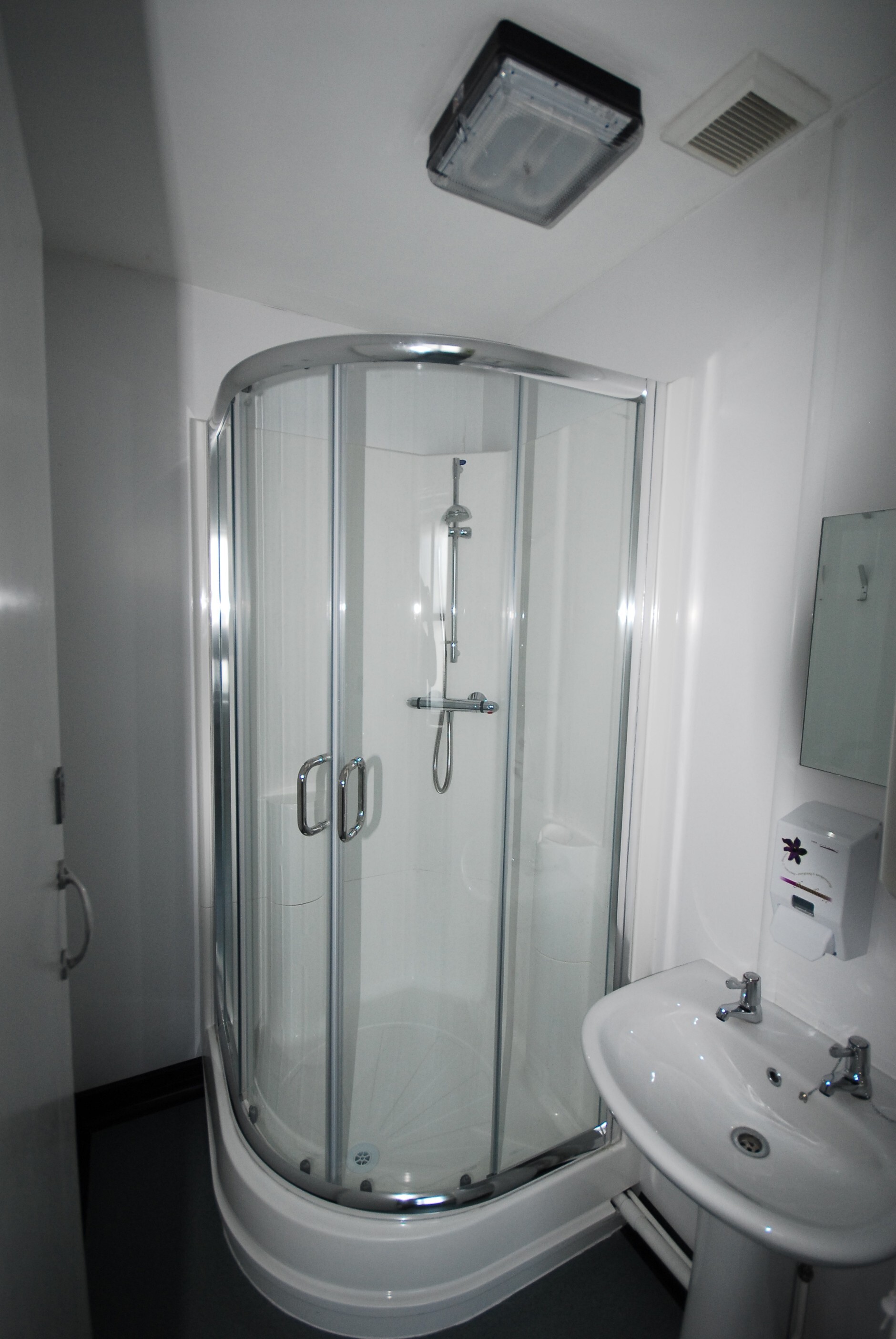 Accessible shower cubicle with curved glass doors, chrome fittings and a built-in shower in a modern bathroom