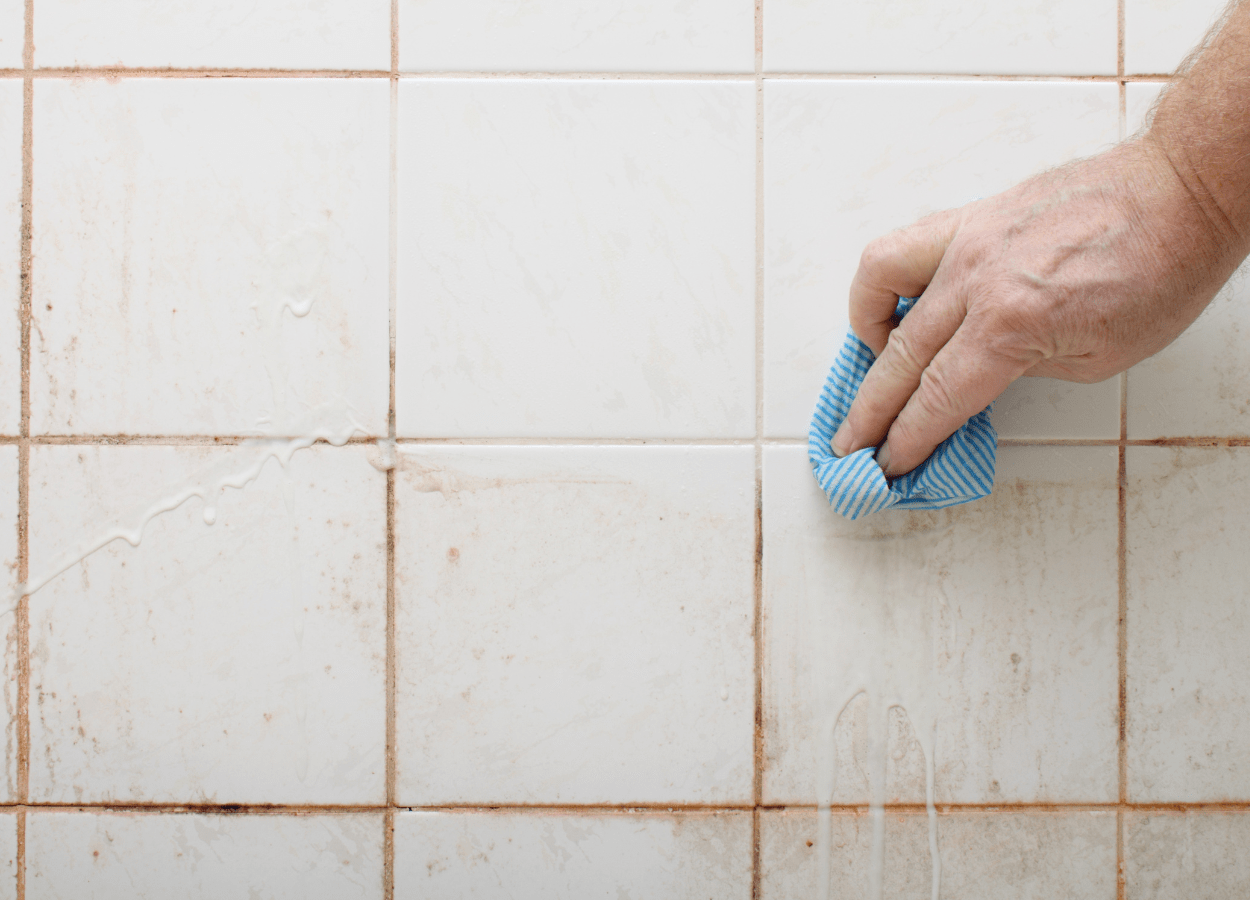 A person getting the mould in their bathroom under control using a cloth and white vinegar.