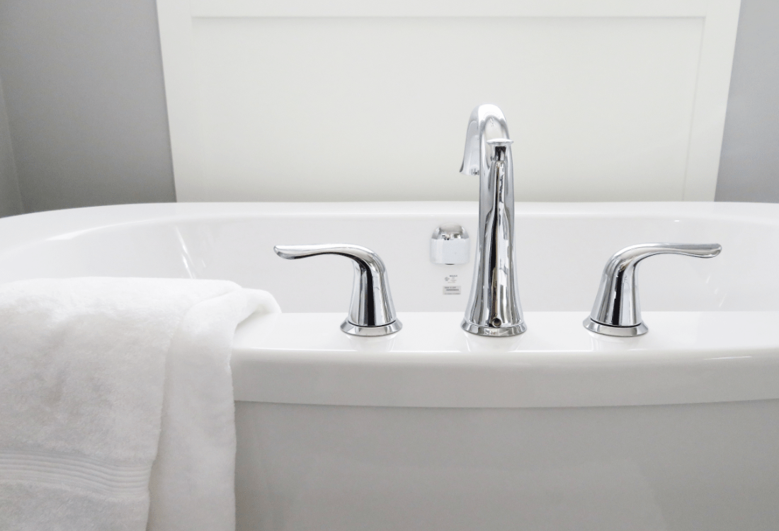 A close up image of a bath, capturing both the hot and cold tap with a folded white towel alongside. 